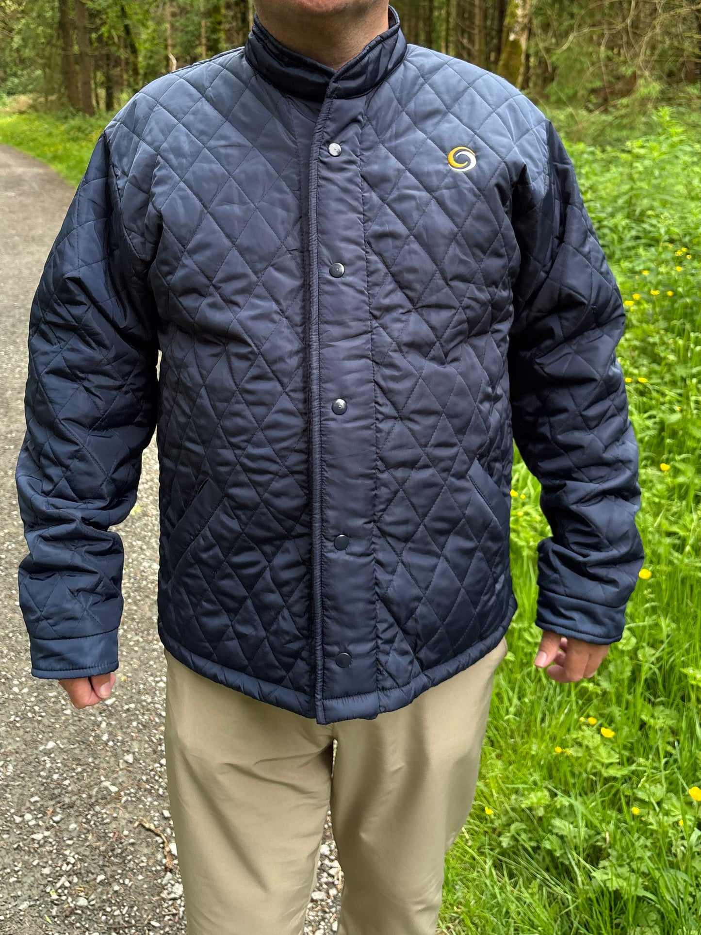 Man wearing a blue quilted jacket standing outdoors with greenery in the background